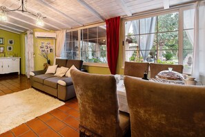 A cozy living room with a sofa, chairs, a dining table, and a large window with curtains. - Annex with Wi-Fi and Air Conditioning (Montegrosso)