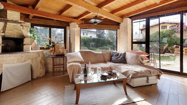 Ein gemütlicher Wohnbereich mit Holzbalkendecke, einem Steinkamin, einem Glastisch und einer Couch.