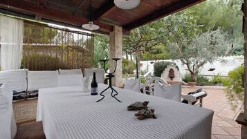 A covered patio with a table set for dining, outdoor seating, and a view of the garden.
