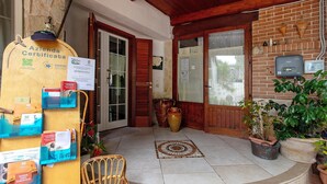 A hotel entrance with a wooden door, a tiled floor, a wicker chair, and a yellow signboard with certificates. - Terrace with Private Terrace, Wi-Fi and Air Conditioning (Montegrosso)