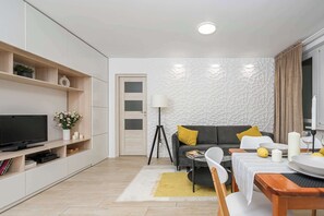 Una sala de estar moderna con un televisor de pantalla plana, un sofá, una mesa de comedor para dos personas y una pequeña mesita auxiliar.