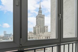 Vista de un edificio imponente a través de una ventana, con cielo despejado y un tren distante.