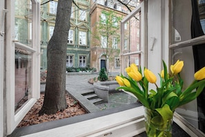 En vy från ett fönster i en byggnad, med ett träd och en blomvas i bild.