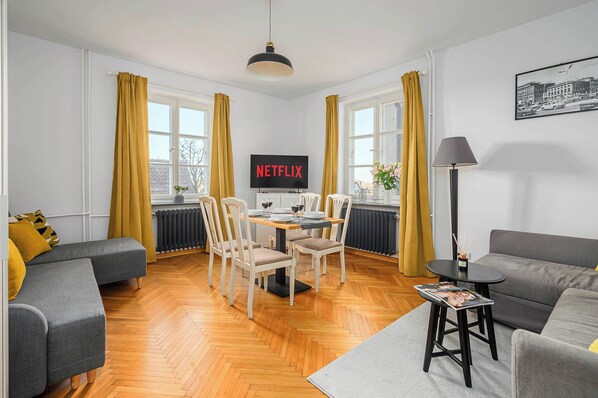 Un salon moderne avec un coin repas, comprenant un téléviseur à écran plat, un plancher en bois et un canapé.