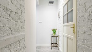 A narrow hallway with white brick walls, a white door with a gold handle, and a small table with a vase of flowers. - Lumina bright apart near the city center (Łódź)