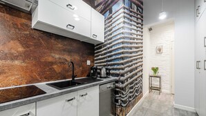 A modern kitchen with a stainless steel sink, white cabinets, and a unique textured wall. - Lumina bright apart near the city center (Łódź)