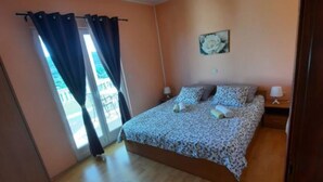 Un dormitorio con cama, dos mesitas de noche, una ventana con cortinas, un tapete pequeño y un cuadro colgado en la pared.