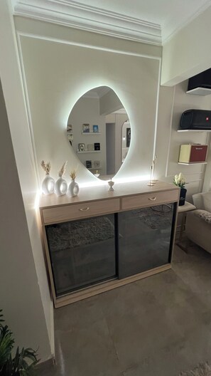 Een kamer met een ronde spiegel boven een console, een bank en een televisie op een plank.