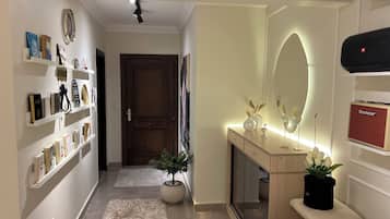 A hallway with a wooden door, a mirror with a light, and a Blackstar speaker on a shelf.