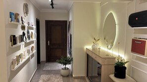 A hallway with a wooden door, a mirror with a light, and a Blackstar speaker on a shelf. - DoUu Stay 1,Luxury 2BR & Office Modern Homes Zayed (El Sheikh Zayed City)