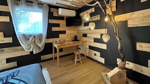 A room with a bed, a desk, and a chair. There is a window with a curtain, and the walls are decorated with wooden panels.
