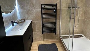 A modern bathroom with a sink, mirror, towel rack, and shower area.