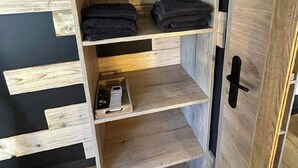 A wooden wardrobe with multiple shelves and a hanging space, containing folded towels and a small electronic device.