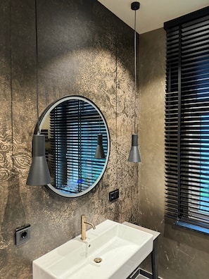 A bathroom with a round mirror, a white sink, and a window with blinds. - Timeless Luxury at the Moated Castle (Neukirchen/Erzgebirge)