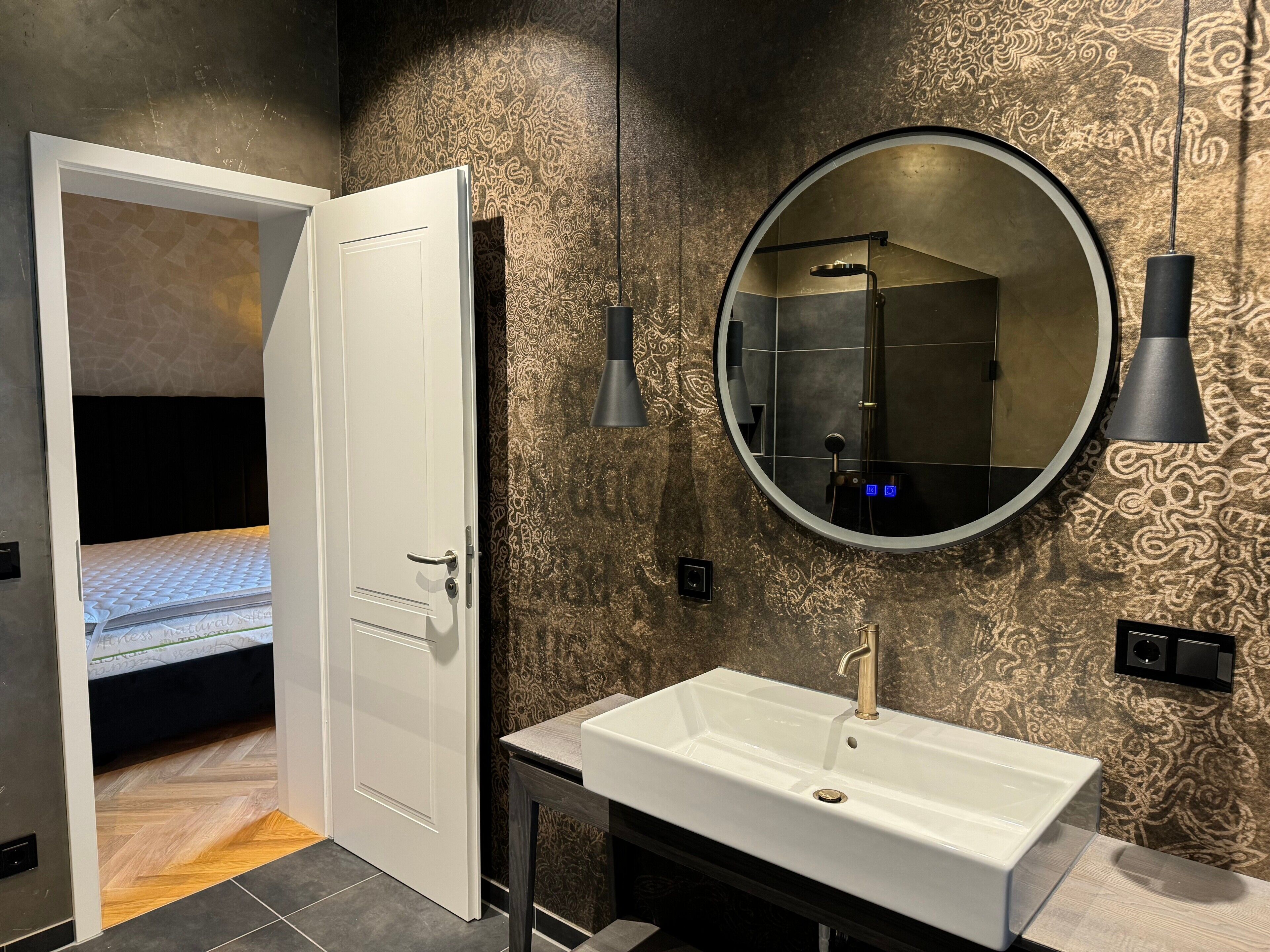 A modern bathroom with a white sink, a round mirror, and a shower.