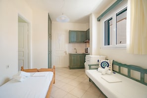 A compact room with a bed, a bench, a small kitchenette, and a door leading to another room. - Odysseia Apartment 1 - 2 Min Walk to Beach, 4 Adults, Terrace, Wi-Fi & AC (Nikiana)