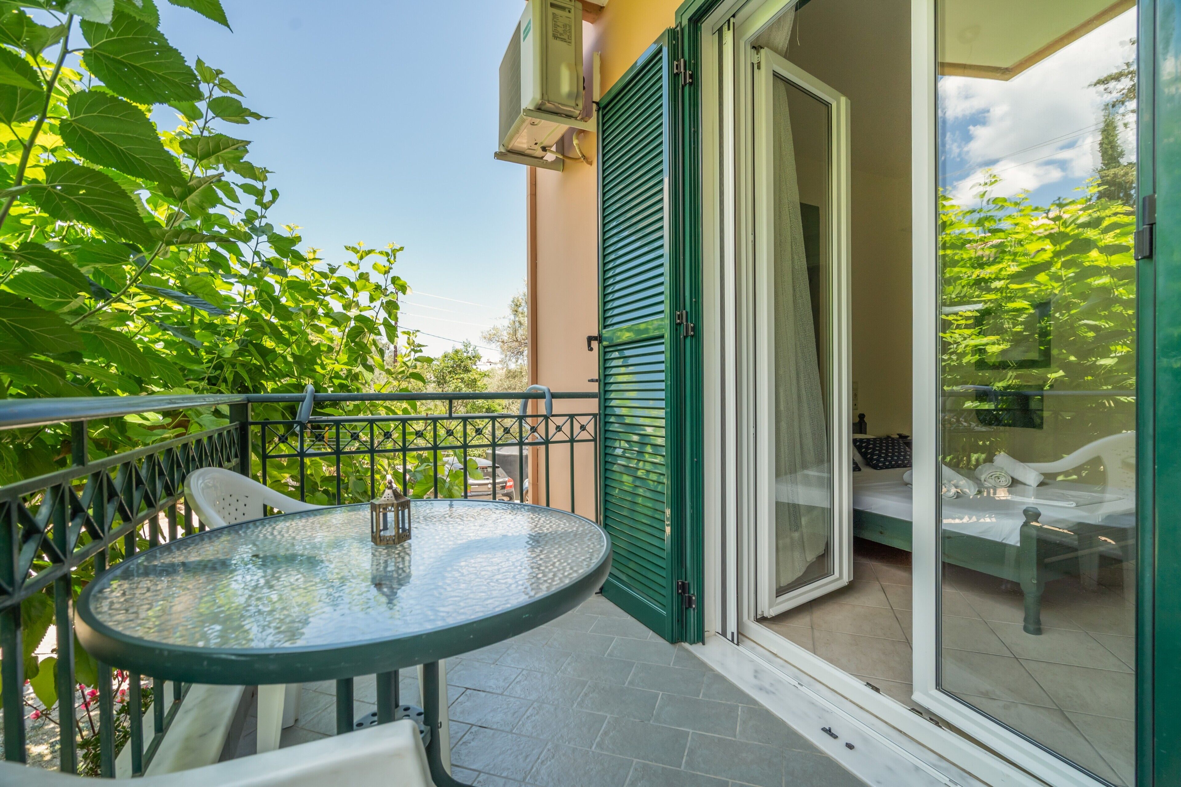 Ein Balkon mit Glastisch und Stühlen, einer Glastür und Blick ins Grüne.