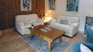 A cozy living room with two white sofas, a wooden coffee table, and three abstract paintings on the walls. - Nethercote Byre (Minehead)