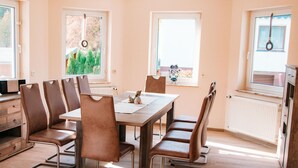 Un área de comedor con una mesa y sillas, una ventana con vista a follaje y un radiador.
