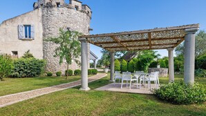 Ein Steinhaus mit einem Turm, einer Pergola mit Stühlen und einem Weg.