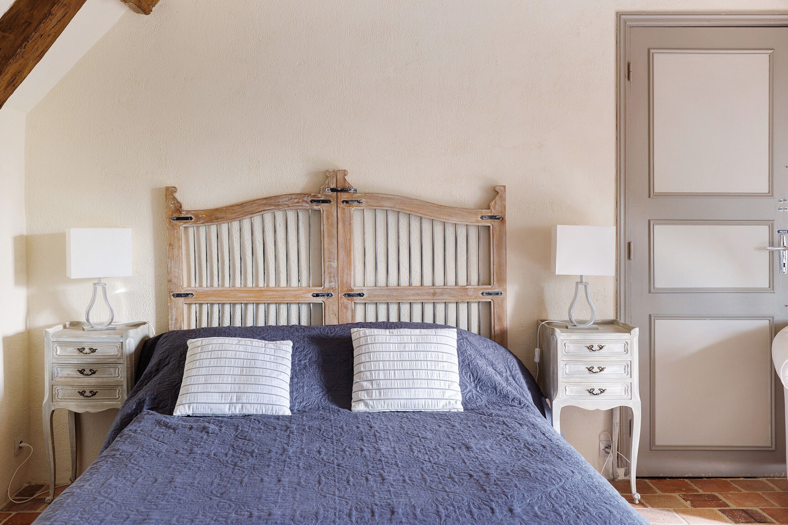 A bed with a wooden headboard, two bedside tables with lamps, and a door to the right.