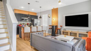 A modern living room with a grey sofa, a dining area with a bar, and a kitchen with a microwave. - Luxury 3BR Home at The Hub Near Disney (Kissimmee)