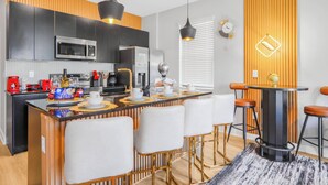 A modern kitchen with a central island, bar stools, and a dining table. - Luxury 3BR Home at The Hub Near Disney (Kissimmee)