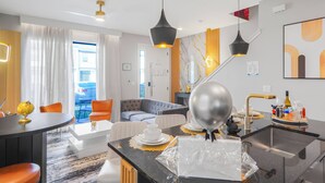 A modern hotel room with a dining area, a sofa, and a kitchen counter. - Luxury 3BR Home at The Hub Near Disney (Kissimmee)
