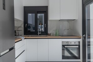 A modern kitchen with a built-in oven, a black-framed window, and a stainless steel refrigerator.