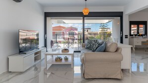 Een moderne woonkamer met een bank, salontafel, televisie en een balkon met uitzicht op gebouwen.