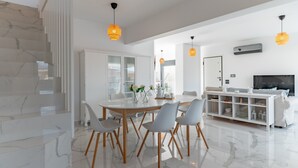 Een moderne woonkamer met een marmeren wenteltrap, een eethoek met een glazen tafel en een televisie op een witte console.