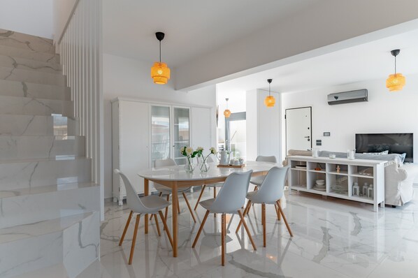 A modern living room with a marble staircase, a dining area with a glass table, and a TV on a white console.