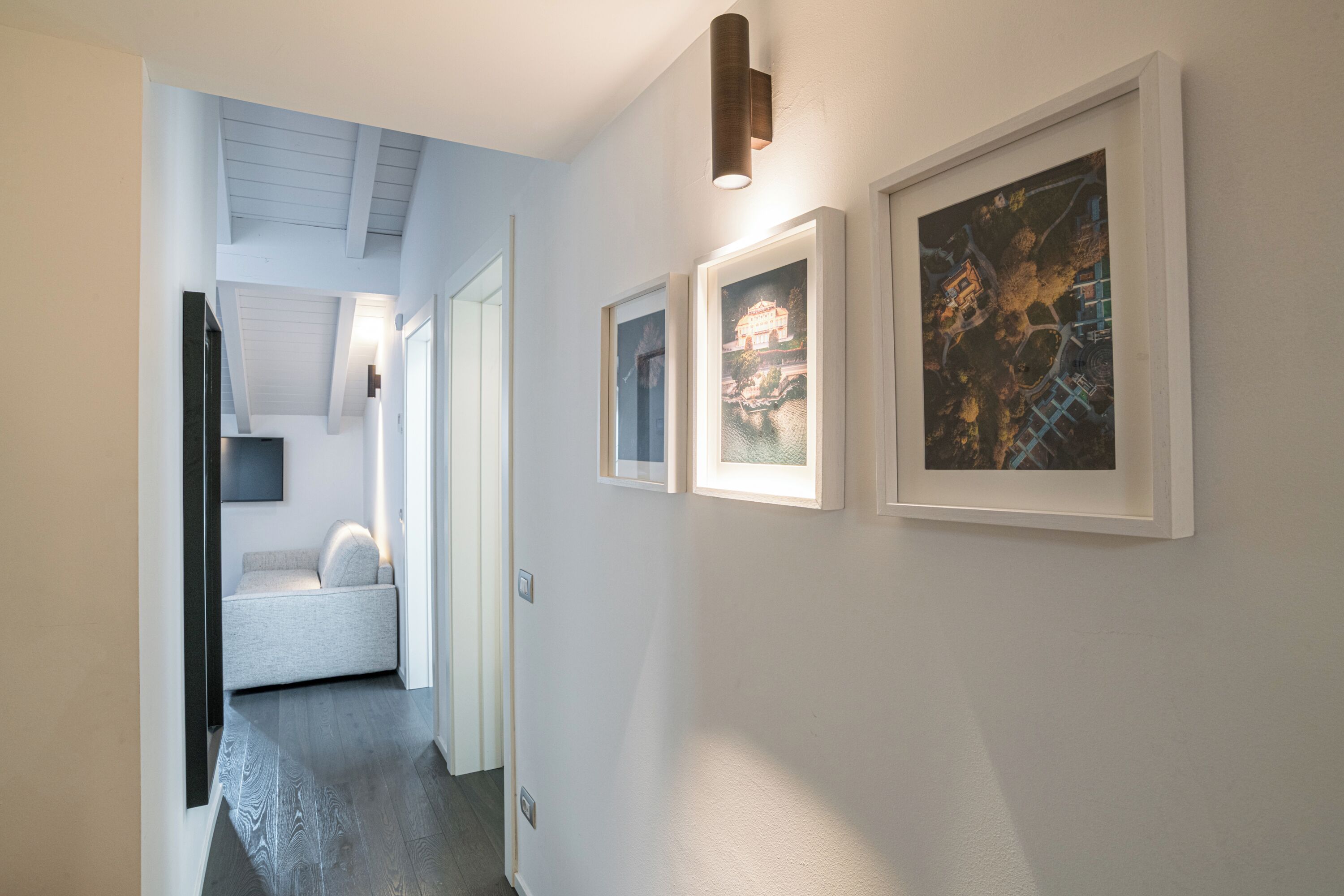 En hall med inramade konstverk på väggarna, en soffa och en taklampa.