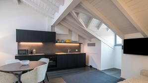 A modern kitchen with dark cabinetry, a dining area with a round table and chairs, and a flat-screen TV mounted on the wall. - Palazzo La Cortesella (Como)