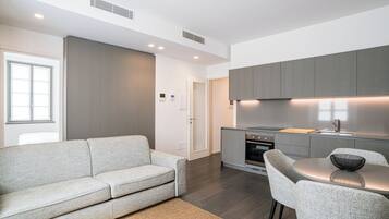 A modern kitchen with grey cabinets, a built-in oven, and a dining area with a round table and grey chairs.