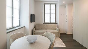 A modern living room with a sofa, a TV mounted on the wall, and a dining table with chairs.