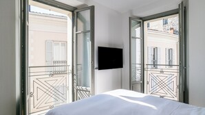 A hotel room with a bed, a TV mounted on the wall, and large windows with a view of buildings. - Palazzo La Cortesella (Como)
