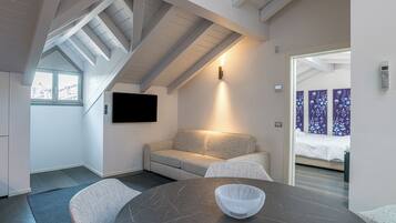 A modern room with a dark marble table, a woven bowl, a grey sofa, and a TV mounted on the wall.