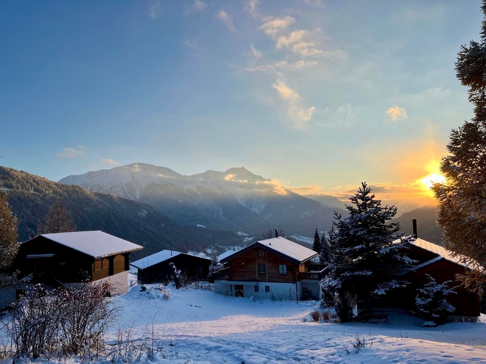 Eine verschneite Berglandschaft mit Holzhütten und blauem Himmel.