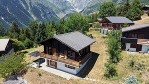 Una baita di legno con un balcone, circondata da montagne e alberi.