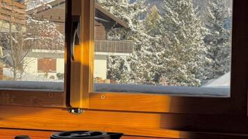 Ein Holztisch mit einer schwarzen Kaffeekanne und zwei Tassen, ein Fenster mit Blick auf schneebedeckte Bäume und Berge.