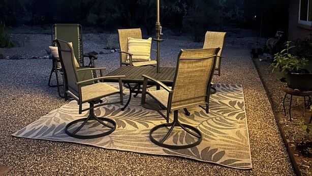 Een terras buiten met een tafel, stoelen, een grote parasol en een grindpad.