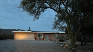 Een gelijkvloers huis met garage, omgeven door een grindpad en schaarse beplanting.