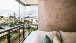 A balcony with a glass railing overlooking a cityscape. - Apartamento Climatizado com Garagem em Alphaville (Barueri)
