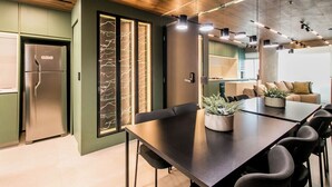 A modern kitchen with a built-in refrigerator, a dining table with chairs, and a decorative wall with a light pattern. - Apartamento Climatizado com Garagem em Alphaville (Barueri)