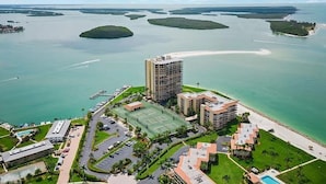 Luchtbeeld van een kusthotel met een groot gebouw, een tennisbaan en een jachthaven.