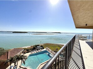Ein Pool mit Meerblick, eine Sonnenterrasse mit Stühlen und ein klarer Himmel.