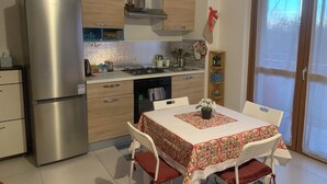 Una cucina moderna con frigorifero in acciaio inossidabile, pensili in legno e piano cottura a gas. Si nota un tavolo da pranzo con sedie e un runner decorativo.