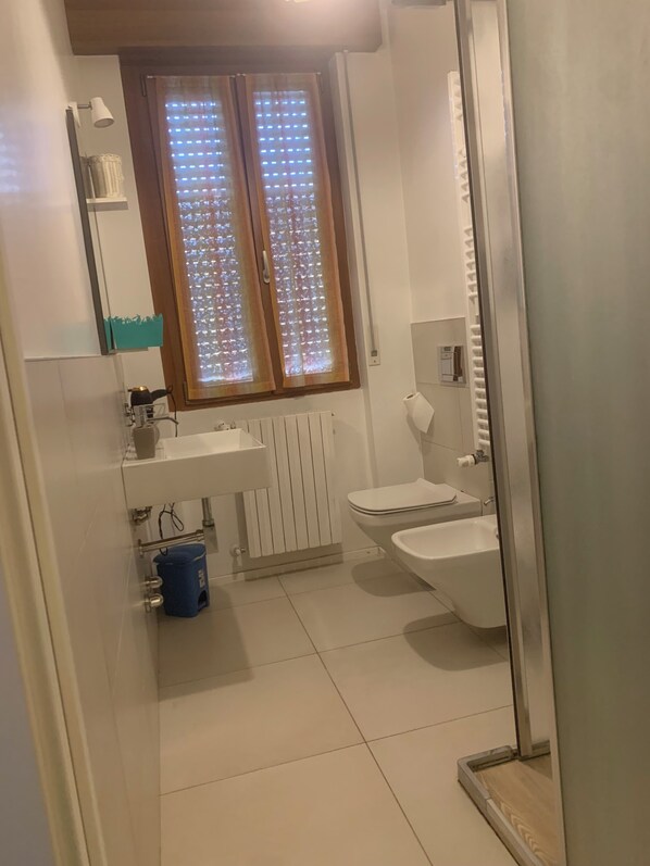 A small bathroom with a toilet, bidet, and a window with a light pattern. - Onlyroomsrho (Rho)