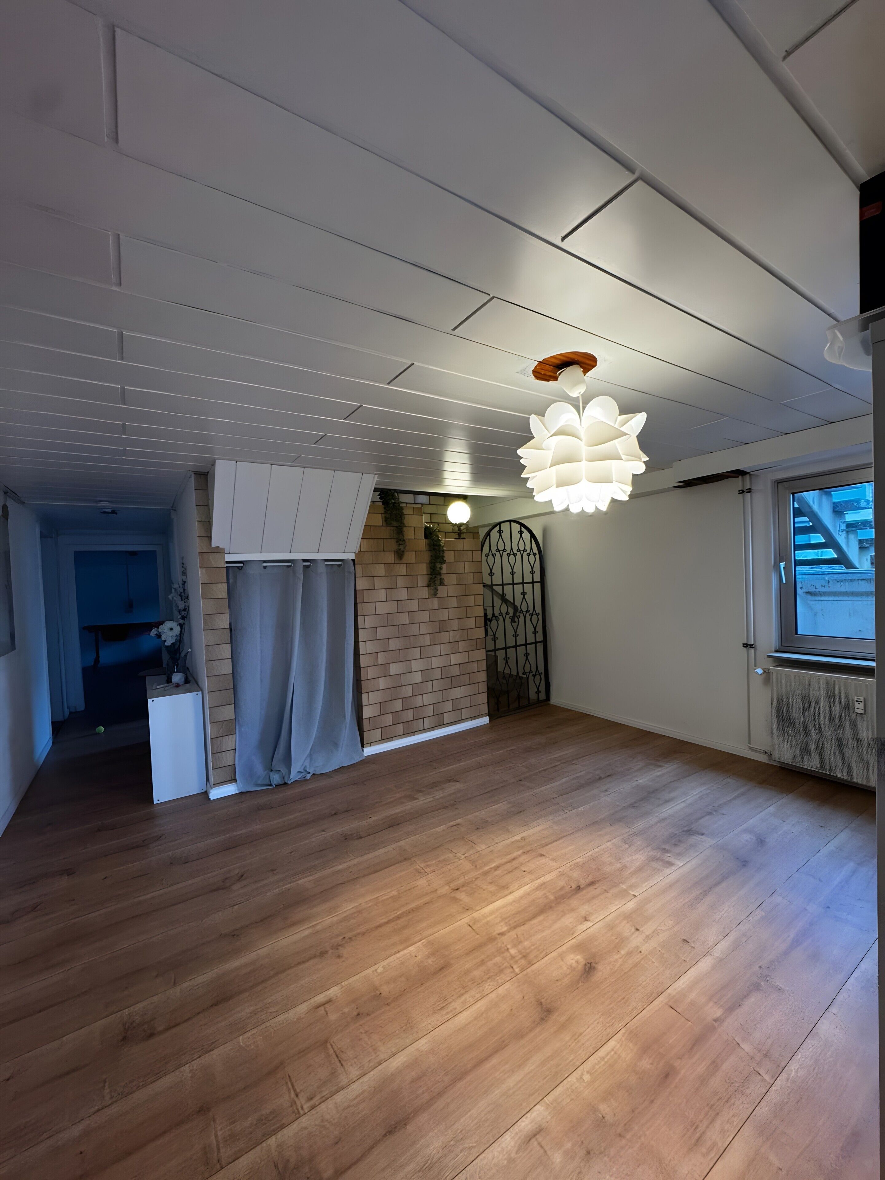 A spacious room with wooden flooring, a white ceiling, and a large window.